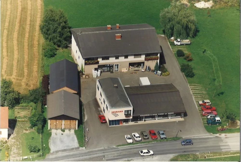 Luftbild des Betriebs mit Wohnhaus, Betriebsgebäude und Parkplatz zwischen Feldern