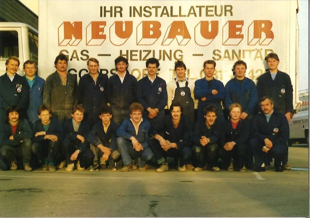 Das Team in blauer Arbeitskleidung vor einem Lastwagen mit der Aufschrift Ihr Installateur Neubauer