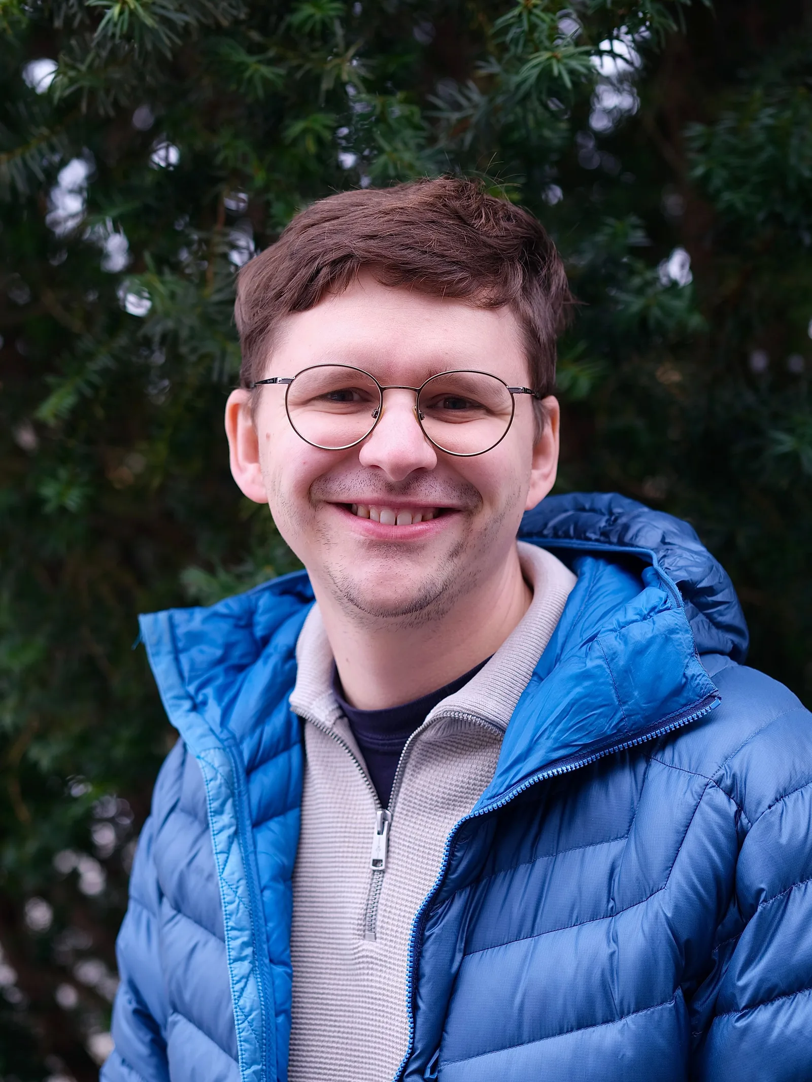Porträt von David Neubauer mit Brille und blauer Jacke vor dunklem Grün