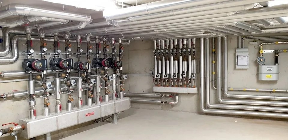 Heizraum mit mehreren Verteilern, Pumpengruppen und gedämmten Leitungen